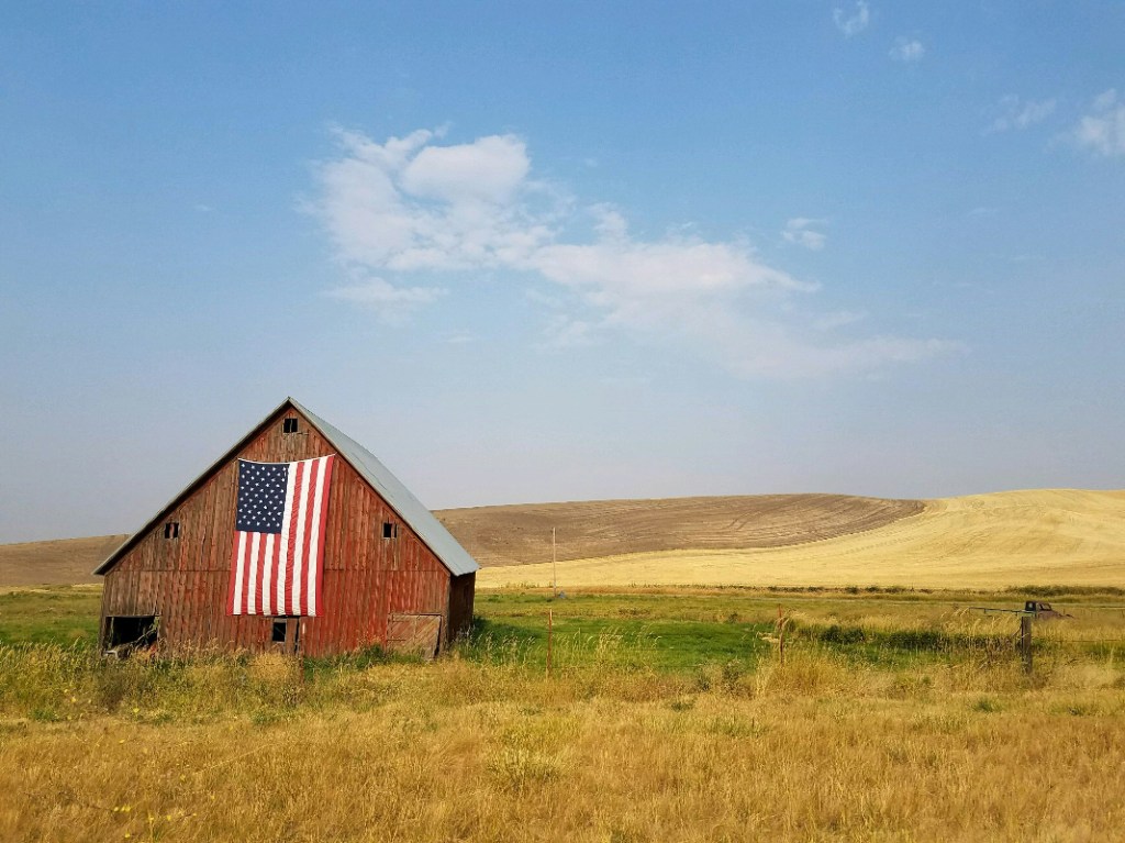 Picture of American flag hanging on a barn with fields in the background
